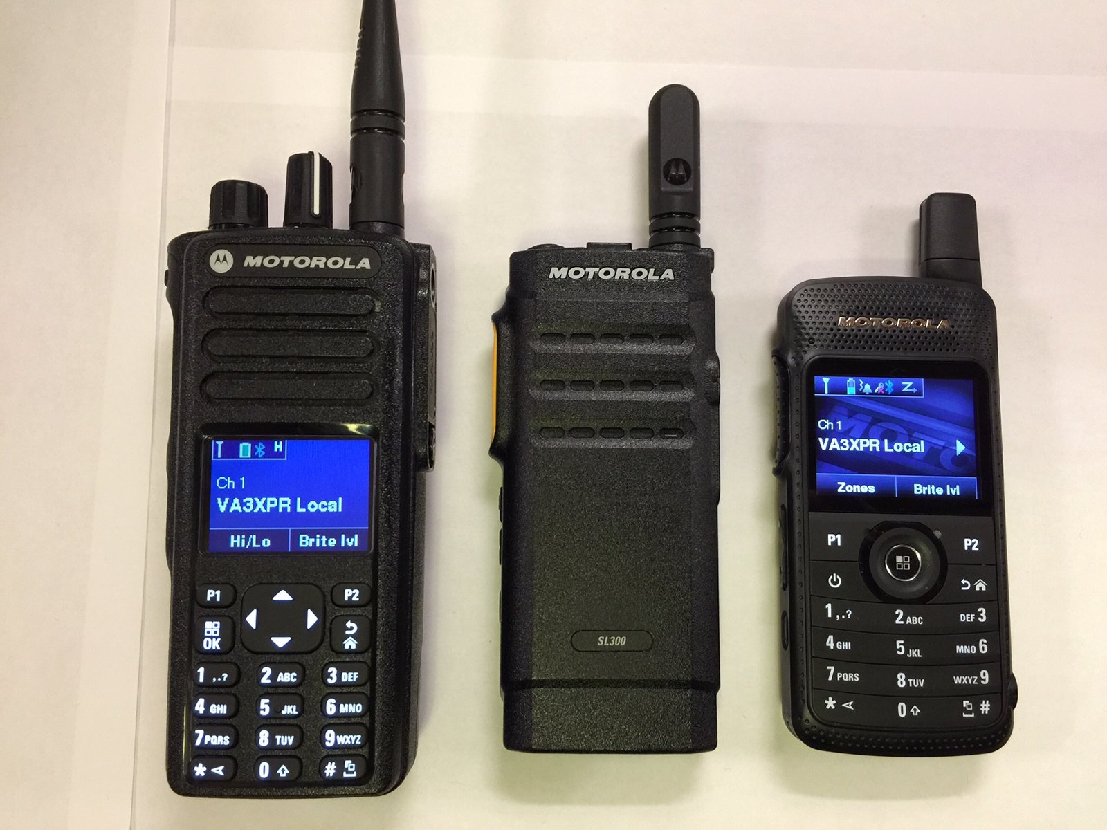 Front view of three Motorola DMR radios aligned side by side—the XPR7550 on the left, the SL300 in the center, and the SL7550 on the right—all displaying their screens.