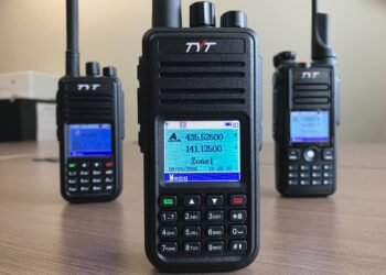 Three budget TYT DMR handheld radios used for digital voice in ham radio, shown on a table with their displays lit.