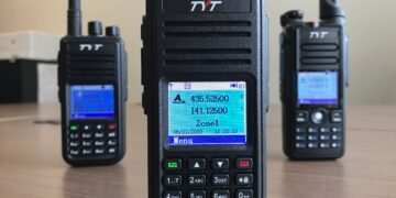 Three budget TYT DMR handheld radios used for digital voice in ham radio, shown on a table with their displays lit.