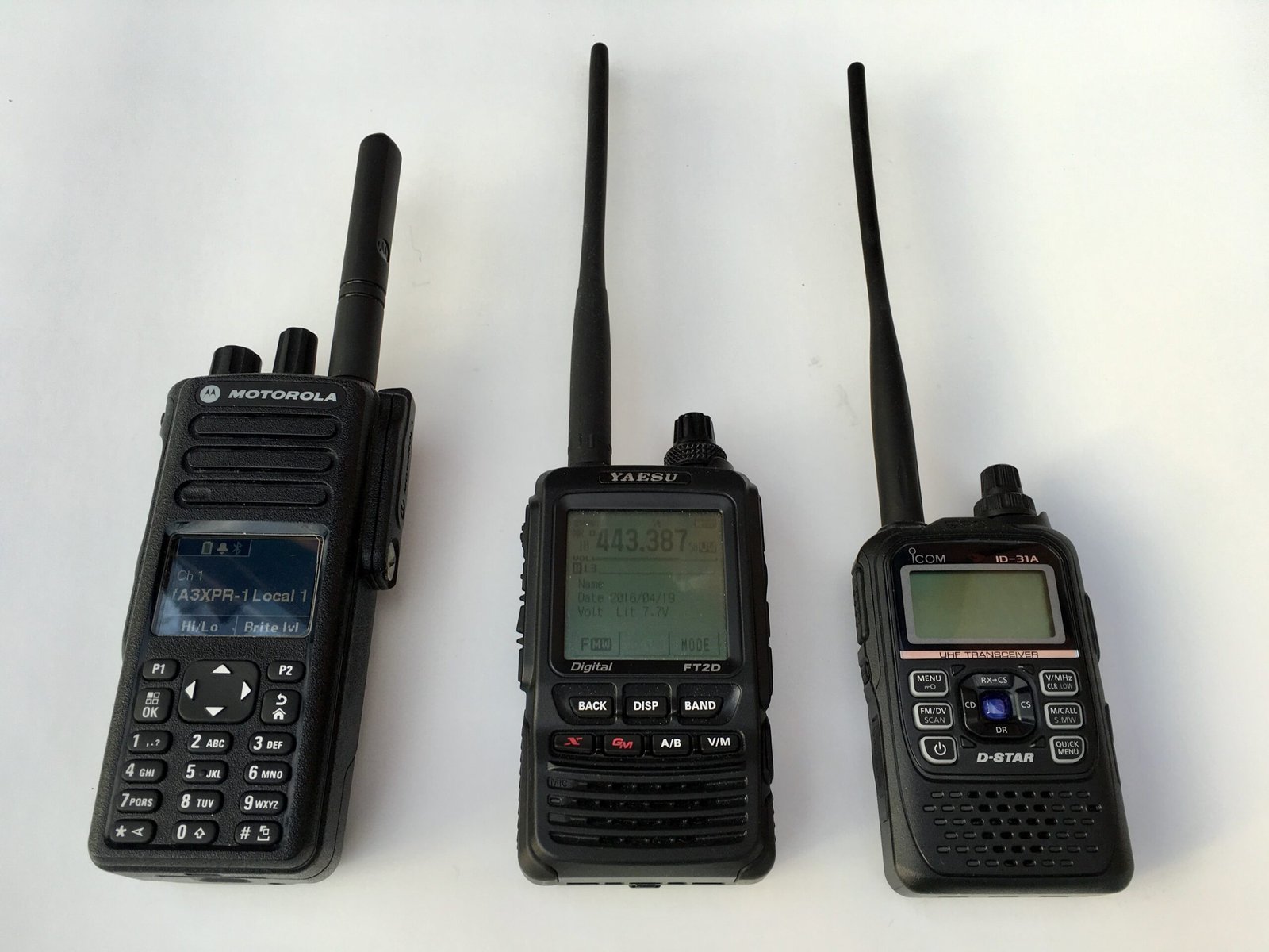 Motorola XPR7550 DMR, Yaesu FT2D System Fusion, and ICOM ID-31A D-STAR handheld ham radios showing the variety of digital voice modes in amateur radio.