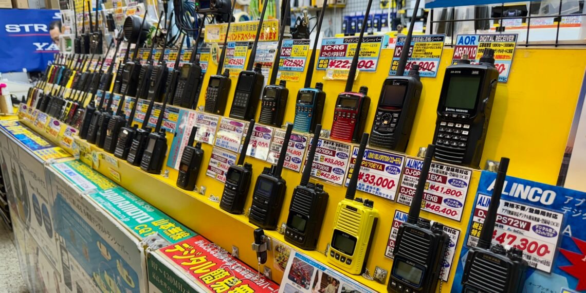 DMR vs Fusion vs D-Star handheld radios on display in an Akihabara ham radio store in Tokyo—rows of analog and digital portable transceivers with price tags.