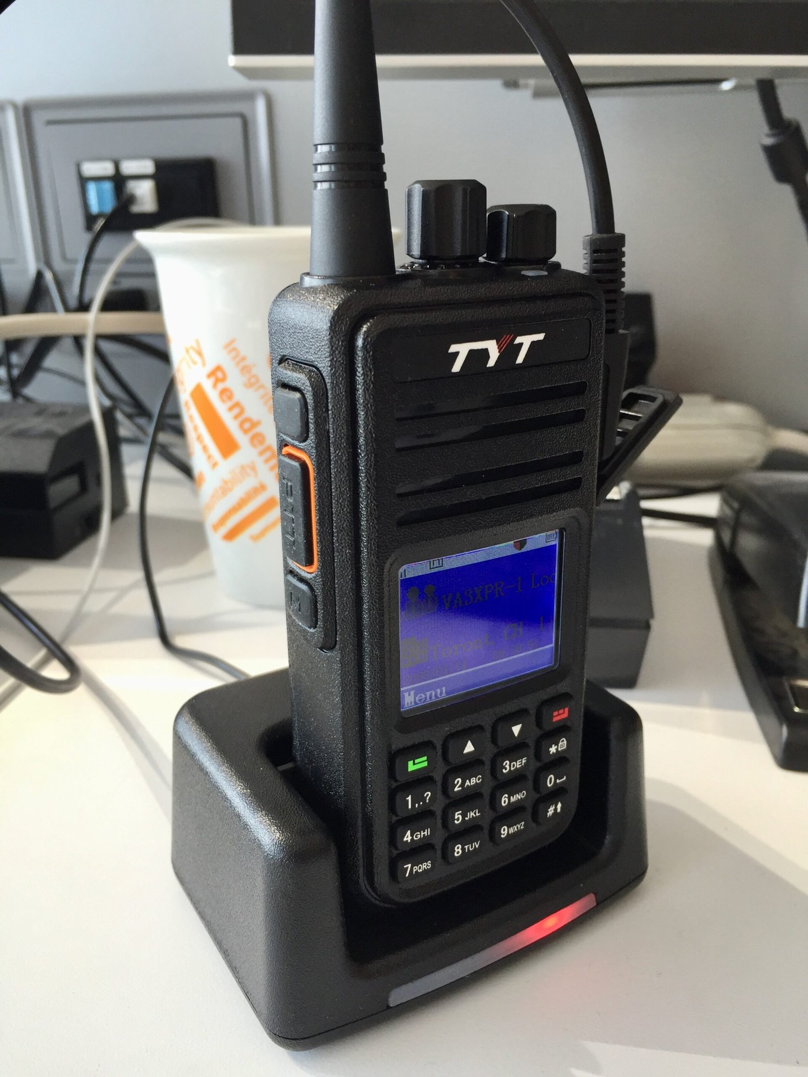 TYT MD-380 UHF DMR handheld radio in its desktop charging cradle with red charging indicator light.