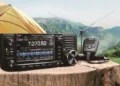 D-STAR for Beginners – Icom IC-705 portable D-STAR radio set up outdoors on a wooden table beside a tent, ready for QRP digital voice operation. Photo credit Icom Inc.